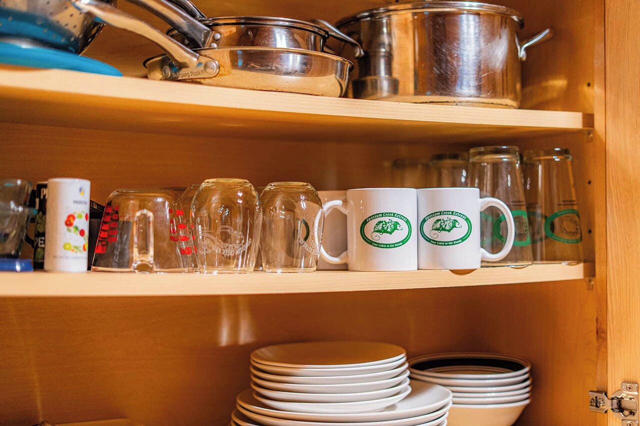Una estantería de cocina con ollas de acero inoxidable, tazas de vidrio y platos apilados.