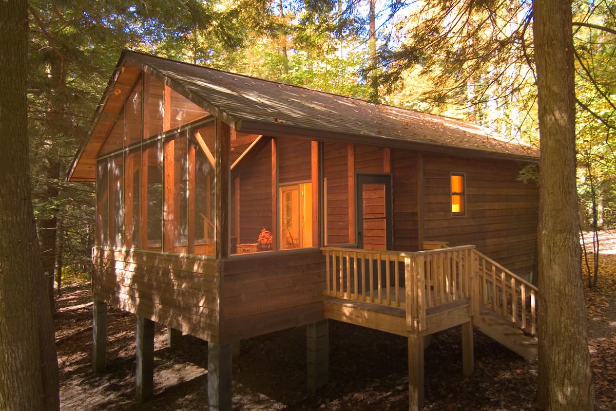 A wooden cabin with a deck and a staircase, surrounded by trees.