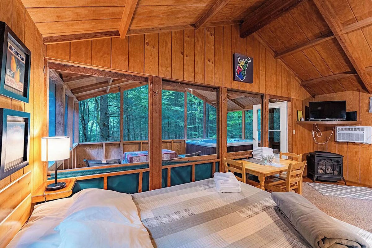 A cabin with a wooden interior, a bed, a table, a television, and a fireplace.