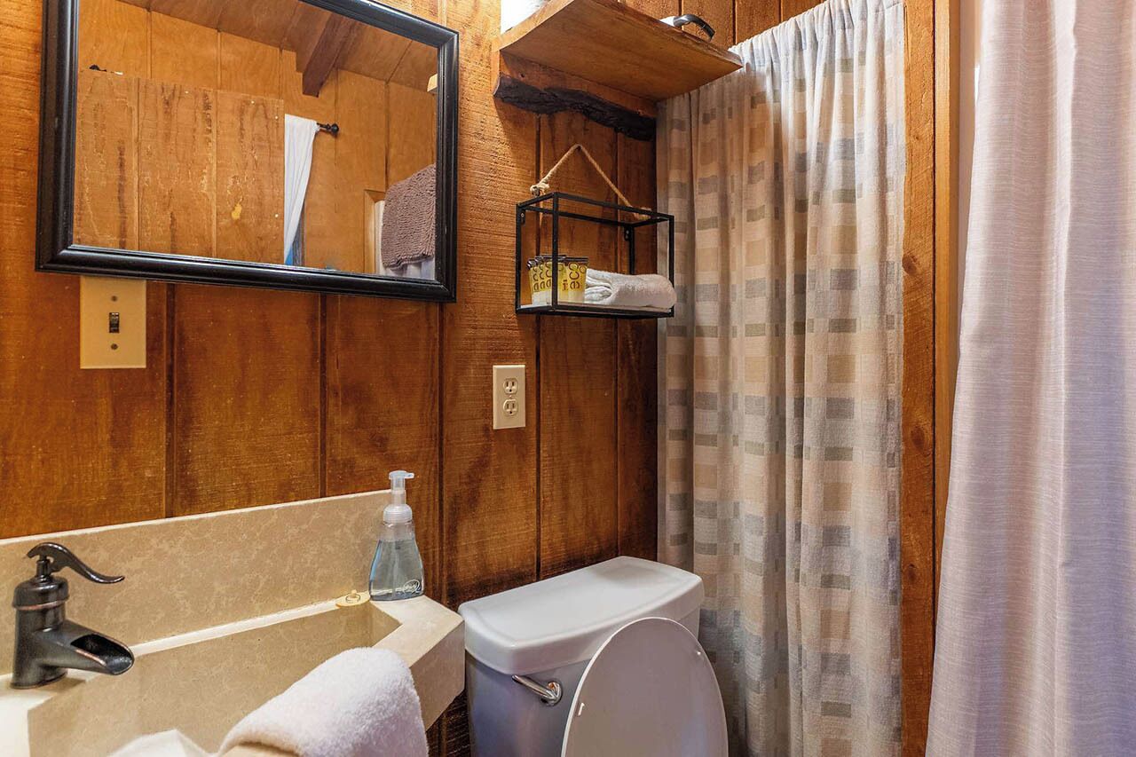 Un baño con paneles de madera, un lavabo, un espejo, un perchero para toallas y un inodoro.