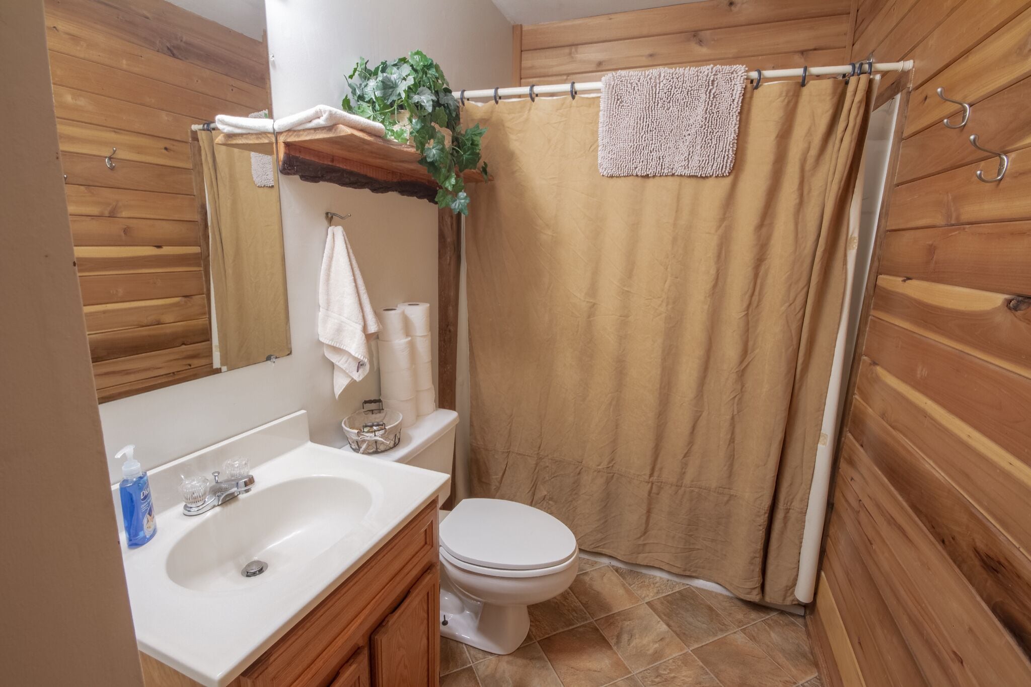 A bathroom with wooden walls, a white sink, a toilet, and a shower curtain.