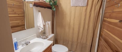 A bathroom with wooden walls, a white sink, a toilet, and a shower curtain.