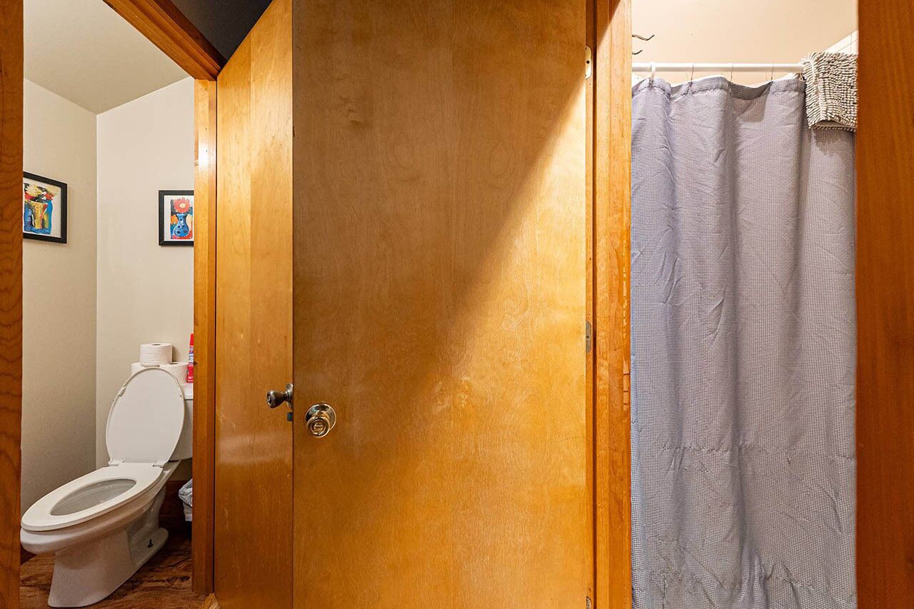 Puerta de madera que da a un baño con inodoro y cortina de ducha.
