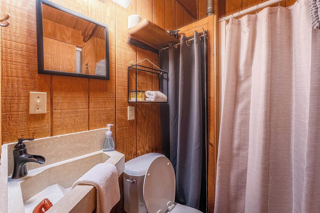 Un baño de madera con lavabo, espejo, inodoro y cortina de ducha.