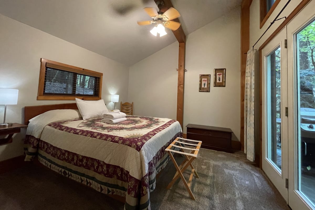A bedroom with a bed, a ceiling fan, a window, and a wooden floor.