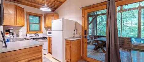 A kitchen with wooden cabinets, a refrigerator, a stove, and a sink. There is a large window with a view of trees.
