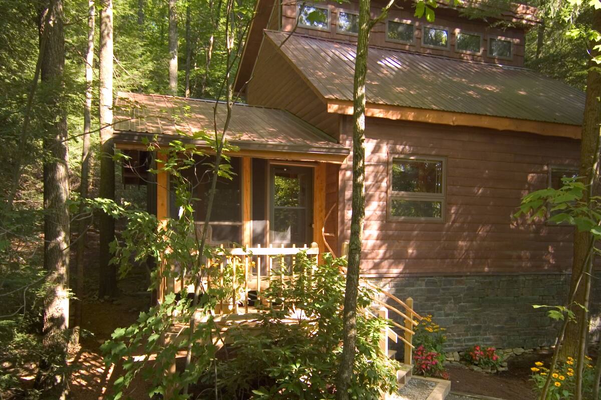 A cabin with a wooden exterior, surrounded by trees and a small garden with flowers.