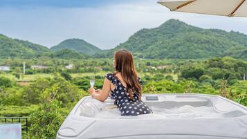 A woman in a polka dot dress sitting in a hot tub with a scenic view of green hills and a clear sky.