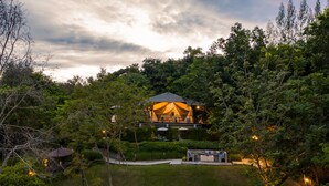 Un refugio apartado rodeado de un bosque denso, con una estructura destacada tipo tienda que tiene techo y un patio.