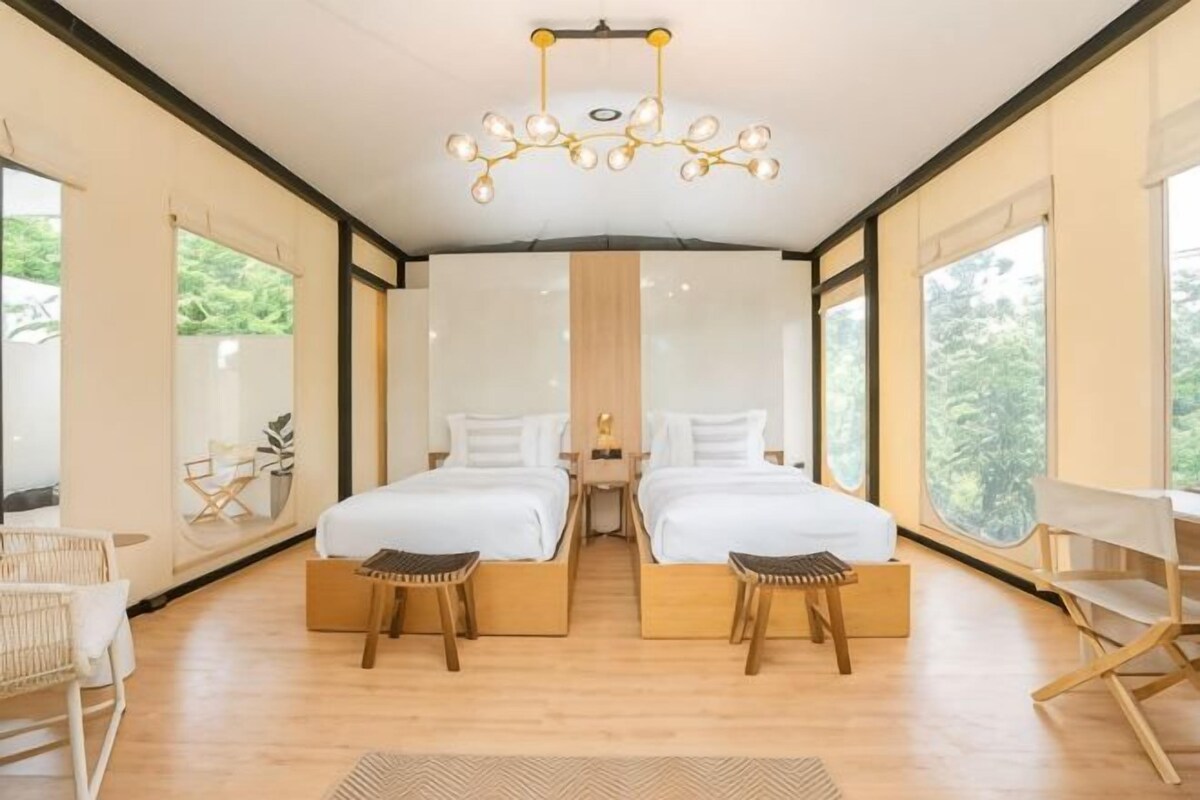 Een moderne slaapkamer met twee bedden, een kroonluchter, grote ramen en een houten vloer.