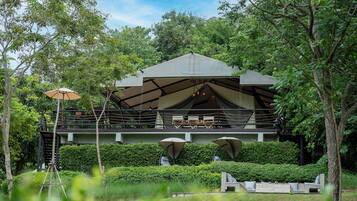 Una estructura moderna al aire libre con un espacio de estar cubierto, rodeada de abundante vegetación y árboles.