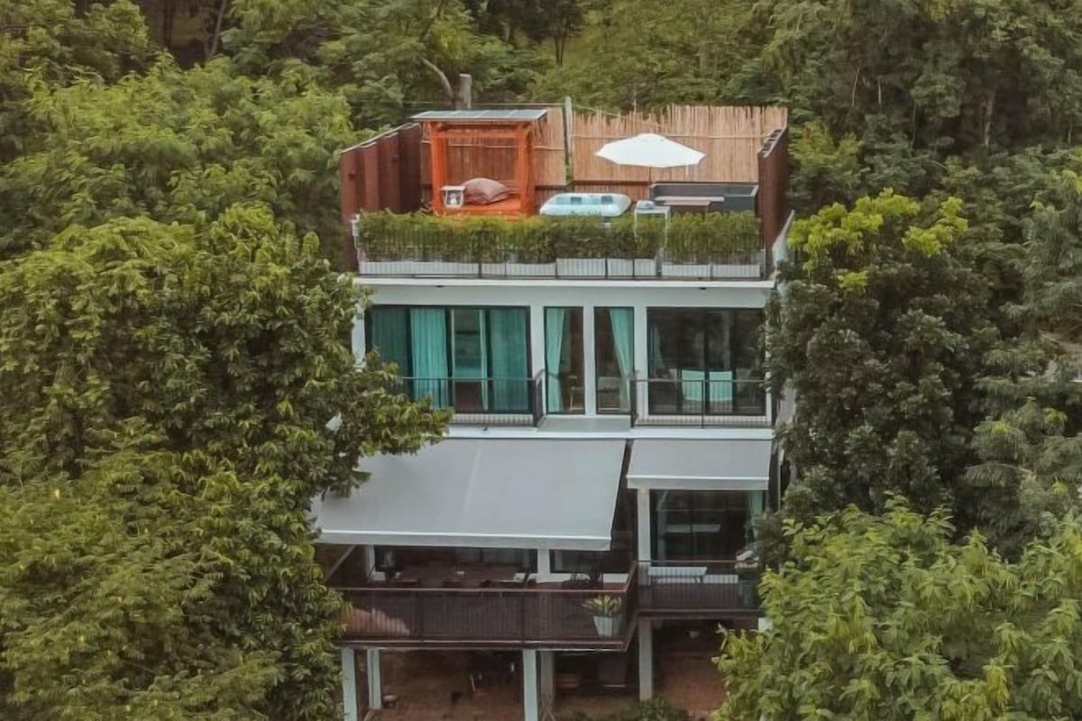 A modern multi-story building with a flat roof, large windows, and a rooftop terrace.
