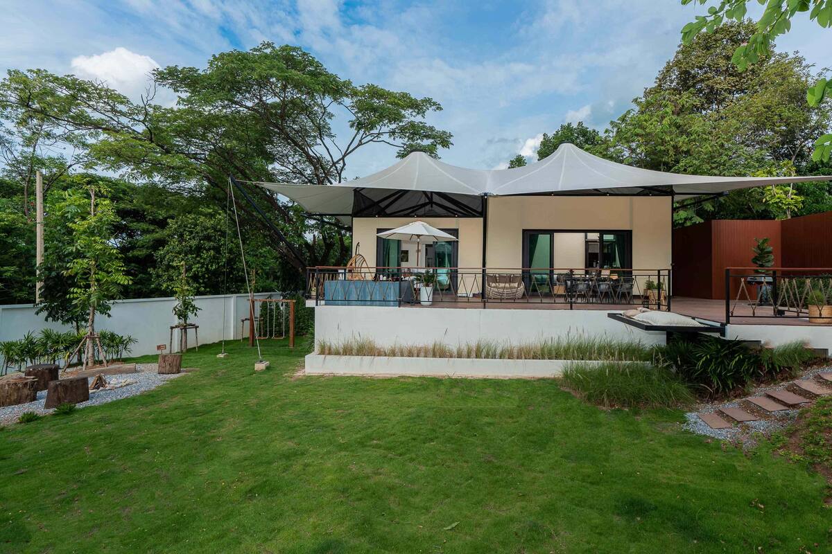 Un patio exterior moderno con una zona de estar cubierta, una piscina y un césped bien cuidado.