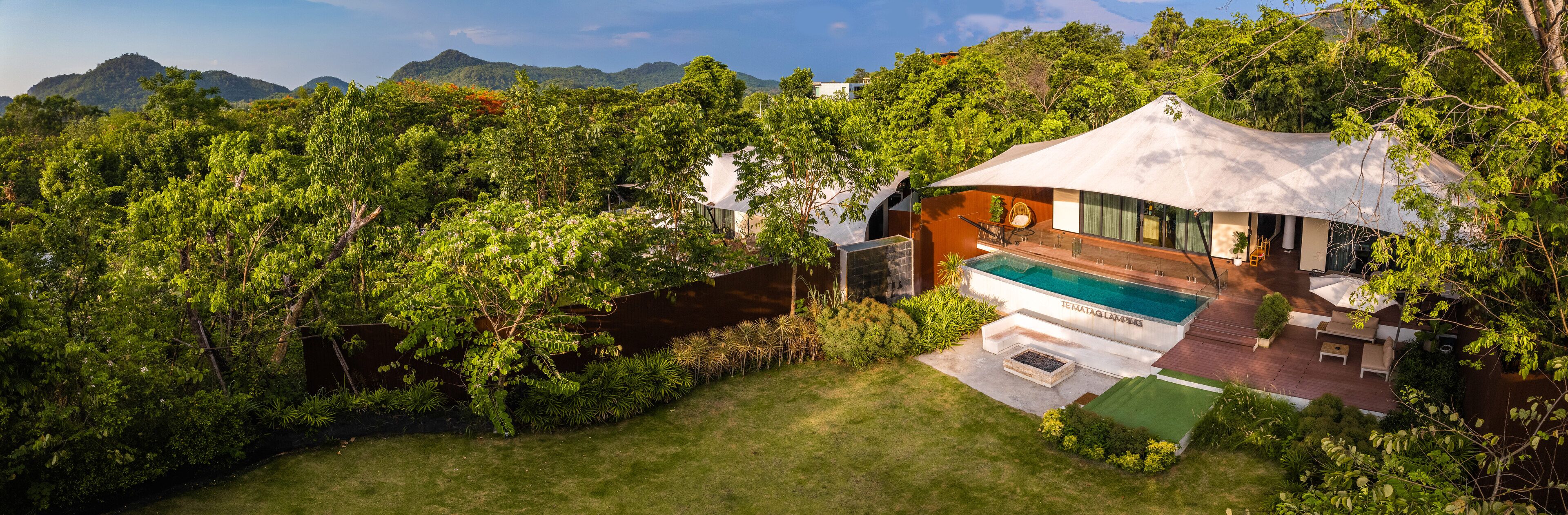 A modern house with a pool, surrounded by lush greenery and mountains in the background.