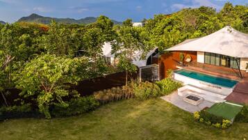 A modern house with a pool, surrounded by lush greenery and mountains in the background.