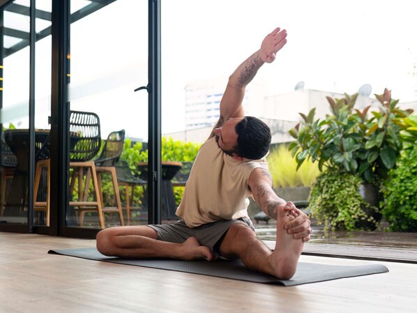 A person performing a yoga pose on a mat indoors with a view of outdoor seating and greenery.