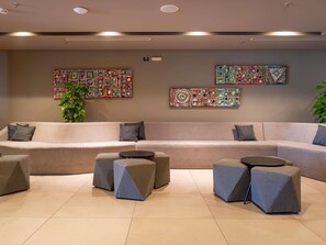A modern living room with a beige sofa, grey ottomans, and abstract wall art. - Novotel Curitiba Batel (Curitiba)