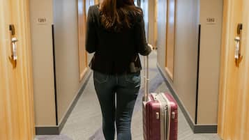 A hotel hallway with doors numbered 1261 and 1262, carpeted floors, and a person walking with a suitcase.