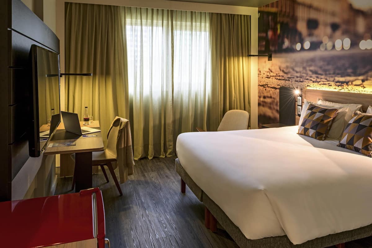 A hotel room with a bed, desk, chair, and a TV.