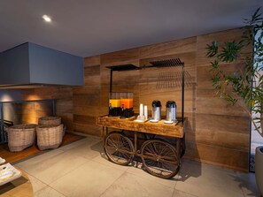 A room with a wooden wall, a cart with coffee makers, baskets, and a plant. - Novotel Curitiba Batel (Curitiba)