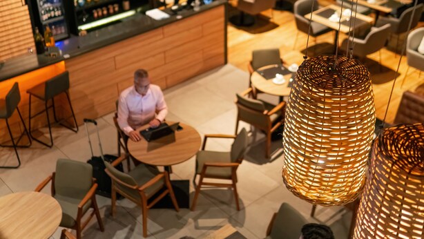 Uma área de bar moderna com balcão de madeira, mesas redondas e cadeiras, além de luminárias trançadas pendentes.