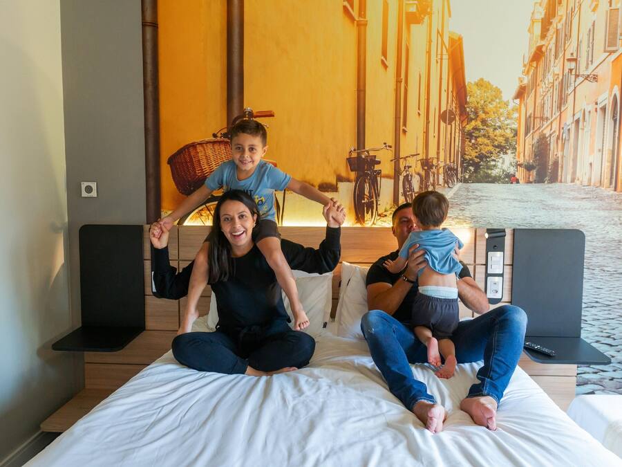 Una cama con un mural de paisaje urbano, cabecera de madera y una mesita con un control remoto.