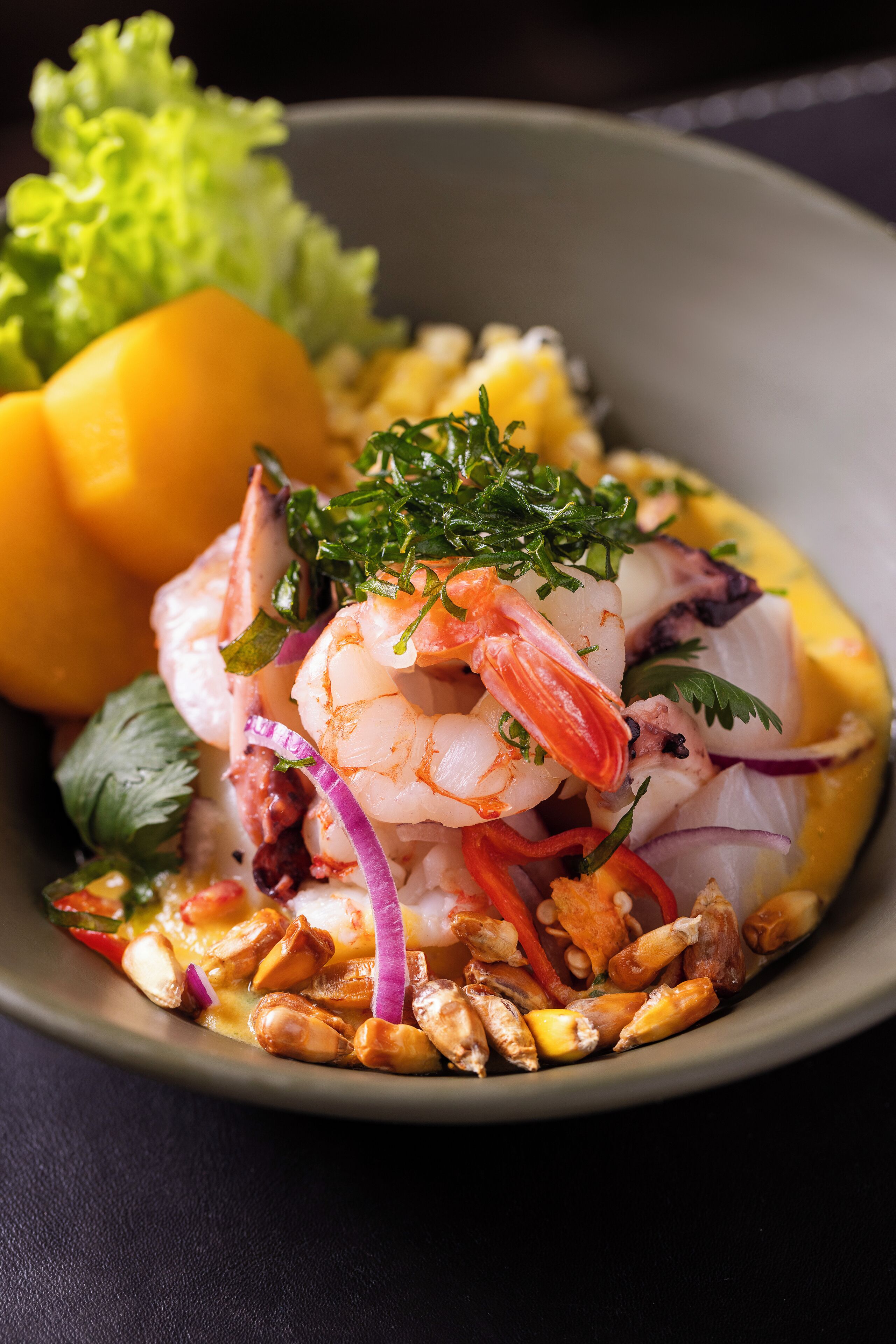 Een kom met garnalen-mango salade, diverse groenten en kruiden.