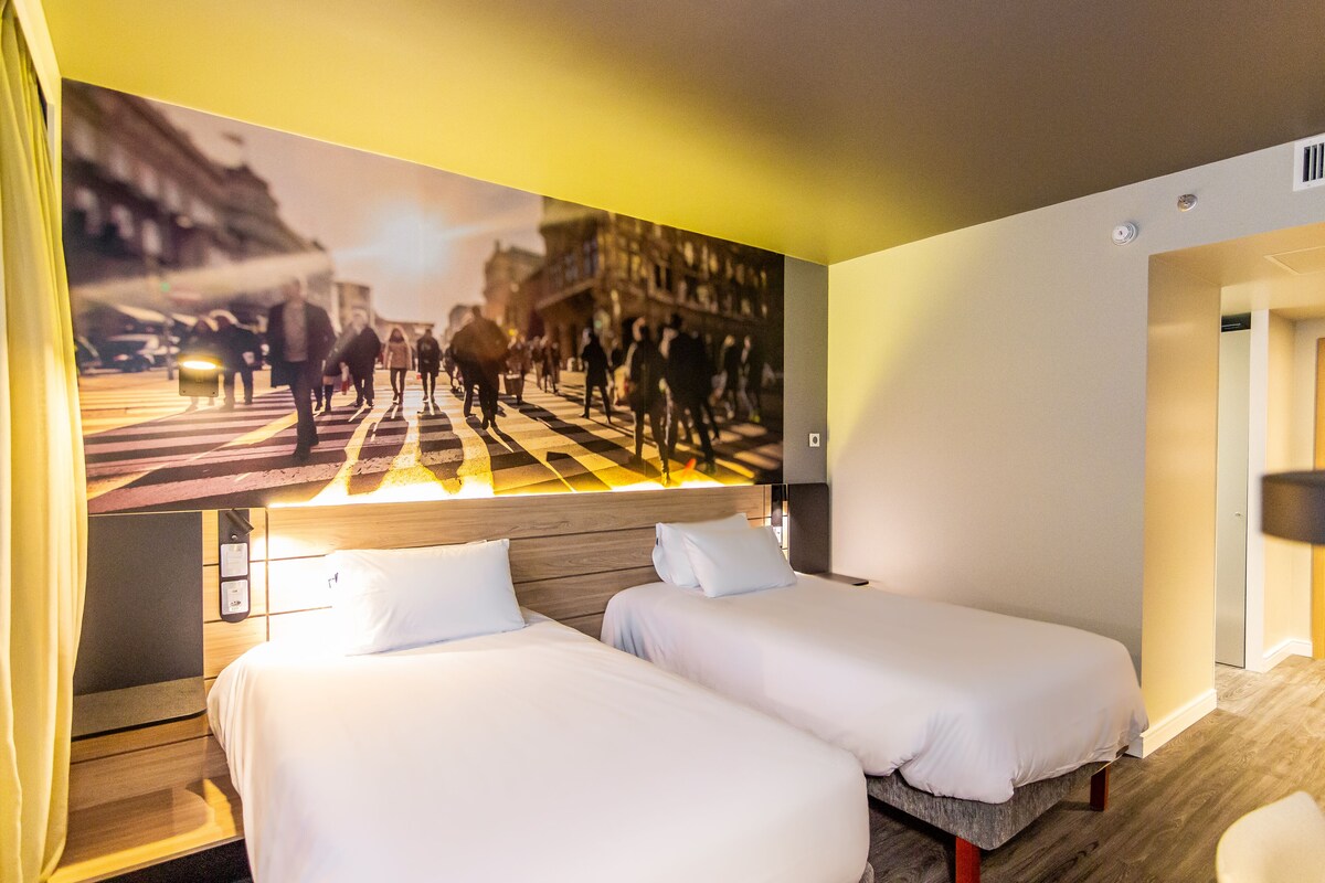 A hotel room with two beds, a large wall mural, and a wooden headboard.
