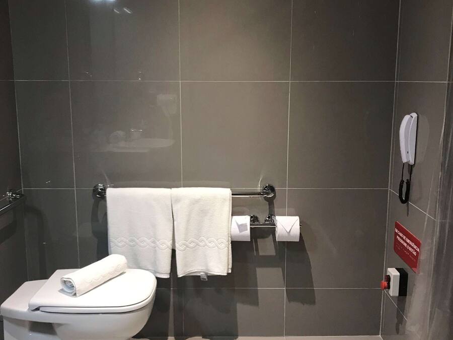 Een moderne badkamer met een toilet, twee handdoeken, een wc-papierhouder en een handdroger.