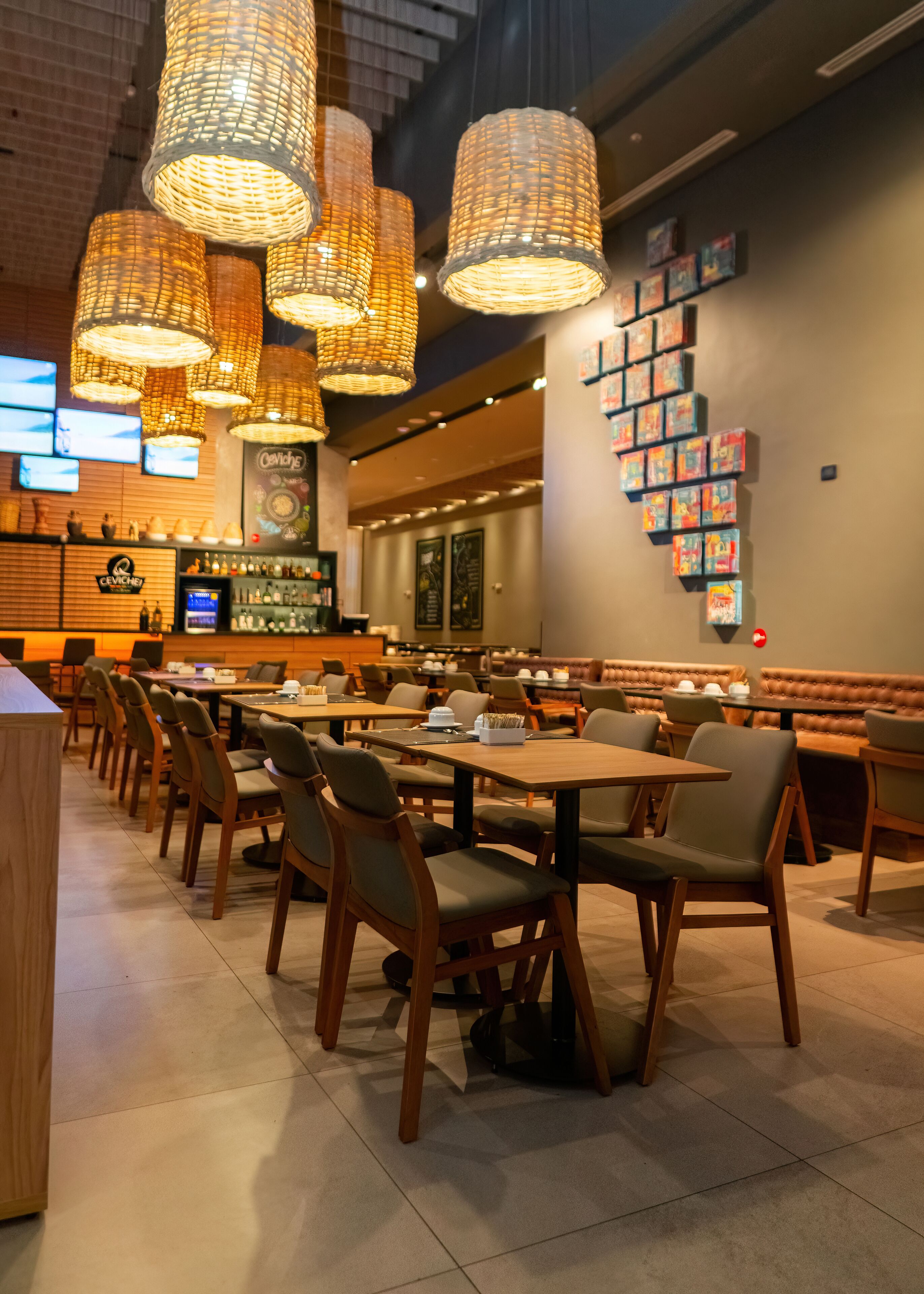 Un restaurante con mesas y sillas de madera, lámparas de mimbre colgantes y una pared con cuadros.
