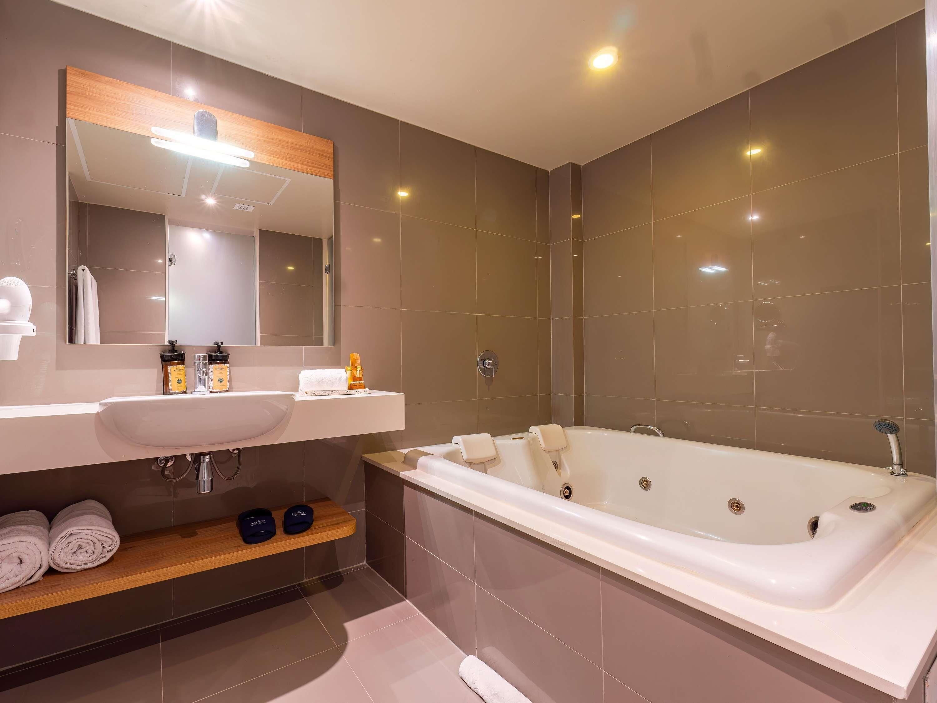 Een moderne badkamer met een groot bad, een wastafel met spiegel en een plank met handdoeken en toiletartikelen.