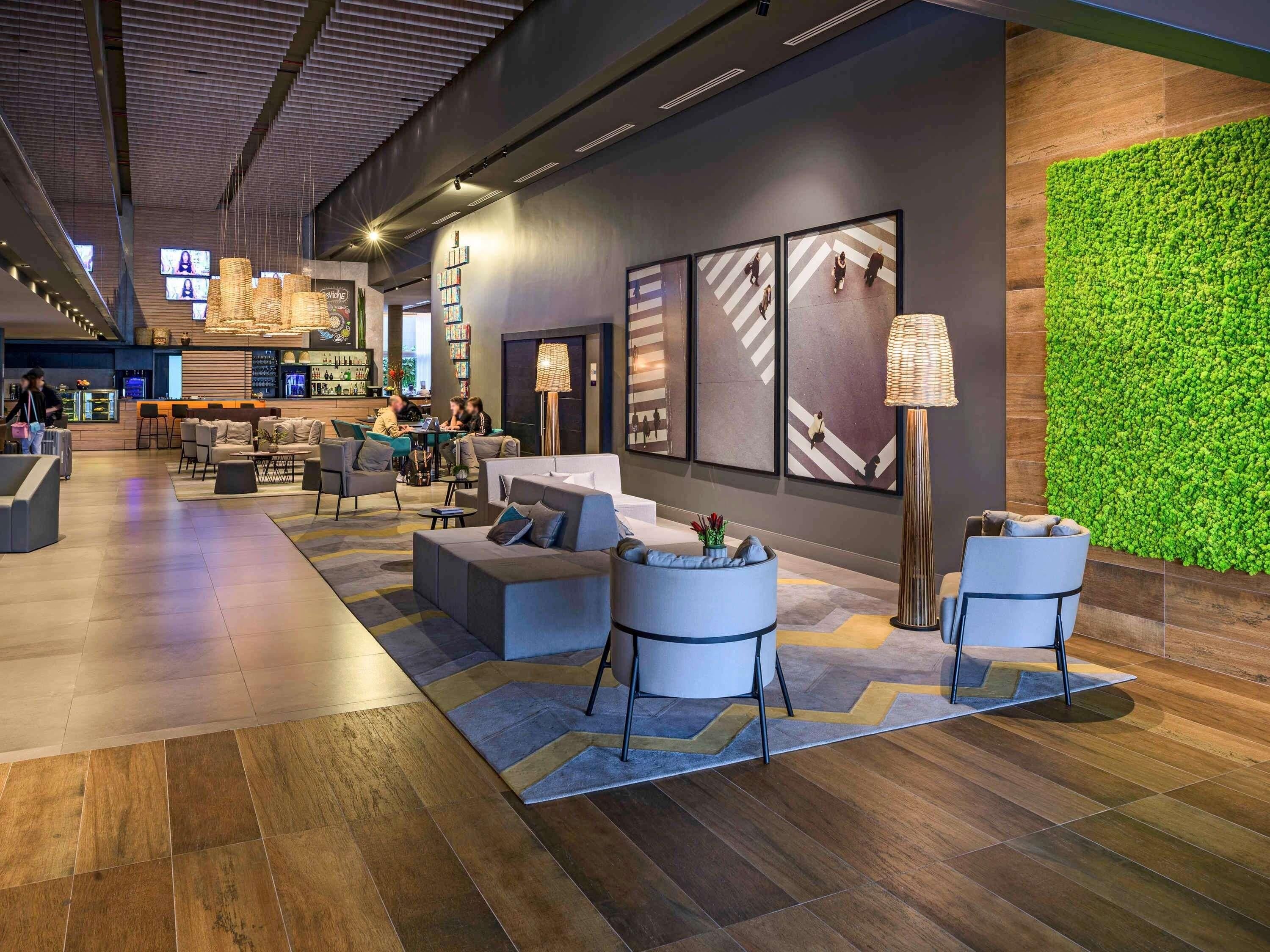 A modern lobby with seating areas, a bar, and a green wall.