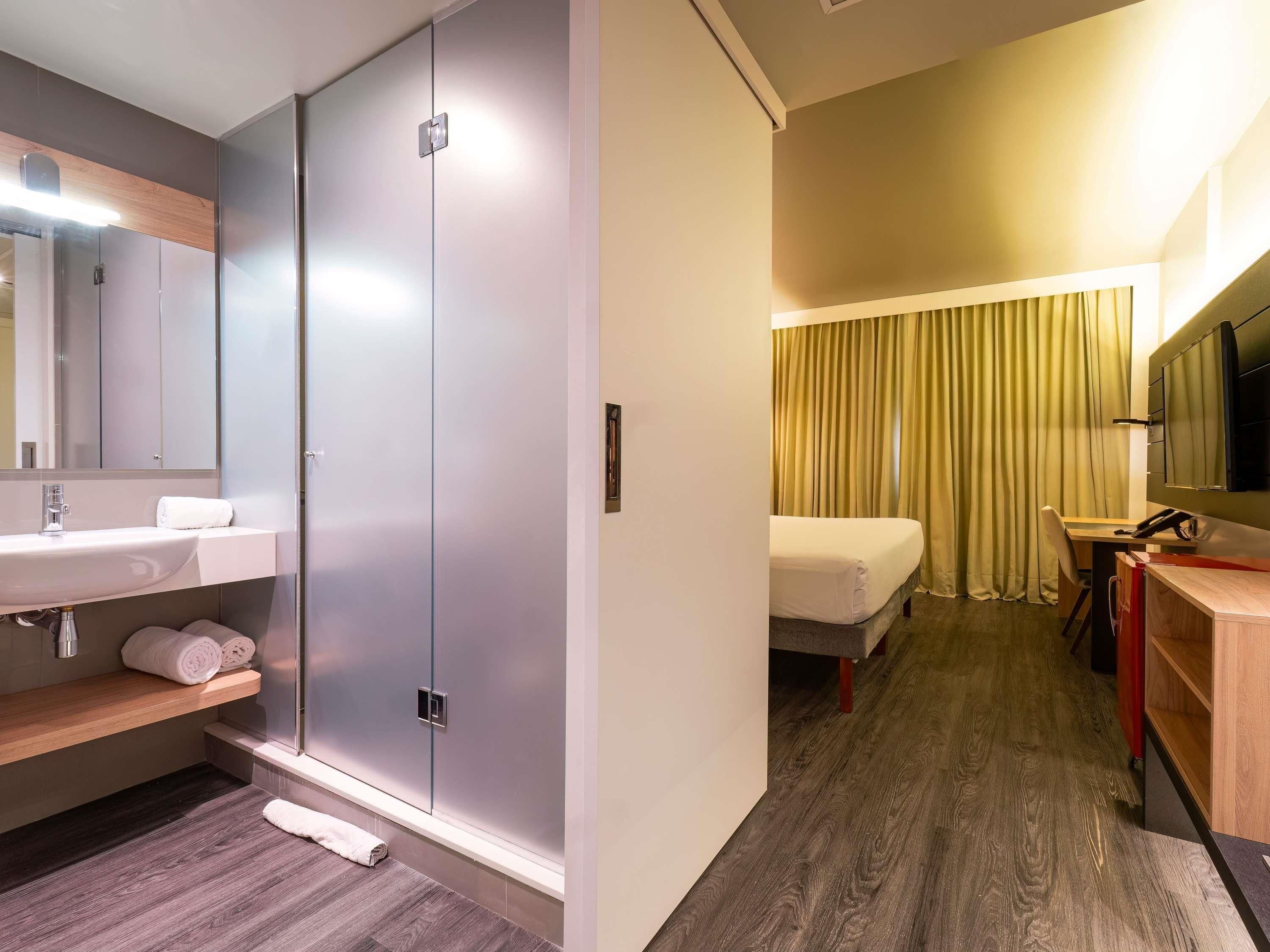 A hotel room with a bathroom, a bed, a desk, and a TV.