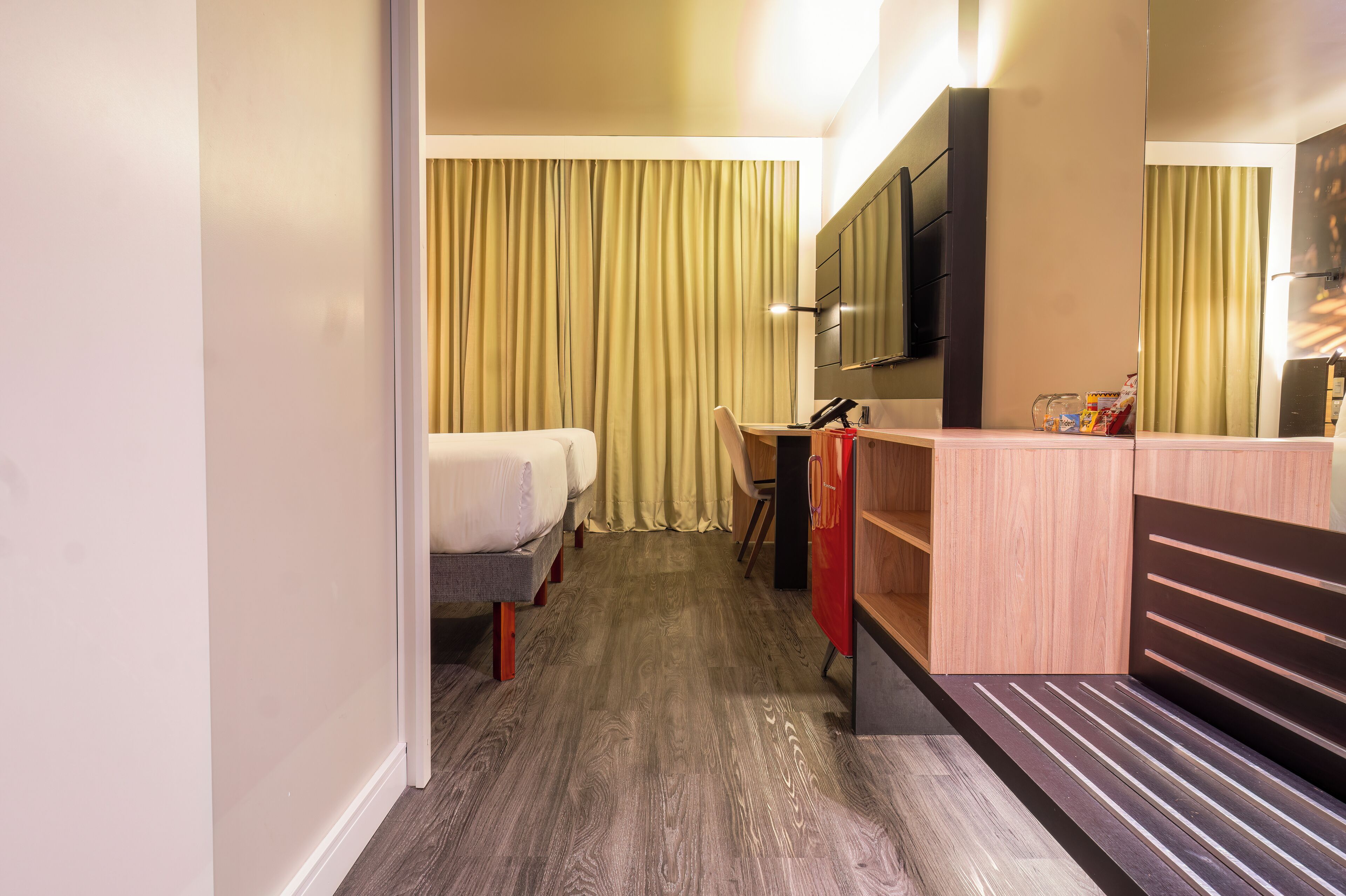 A hotel room with a bed, a desk, a chair, a TV, and a mirror.