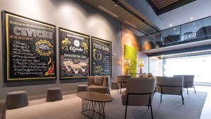 A modern interior with a seating area, a wall with framed artwork, and a staircase leading to an upper level. - Novotel Curitiba Batel (Curitiba)