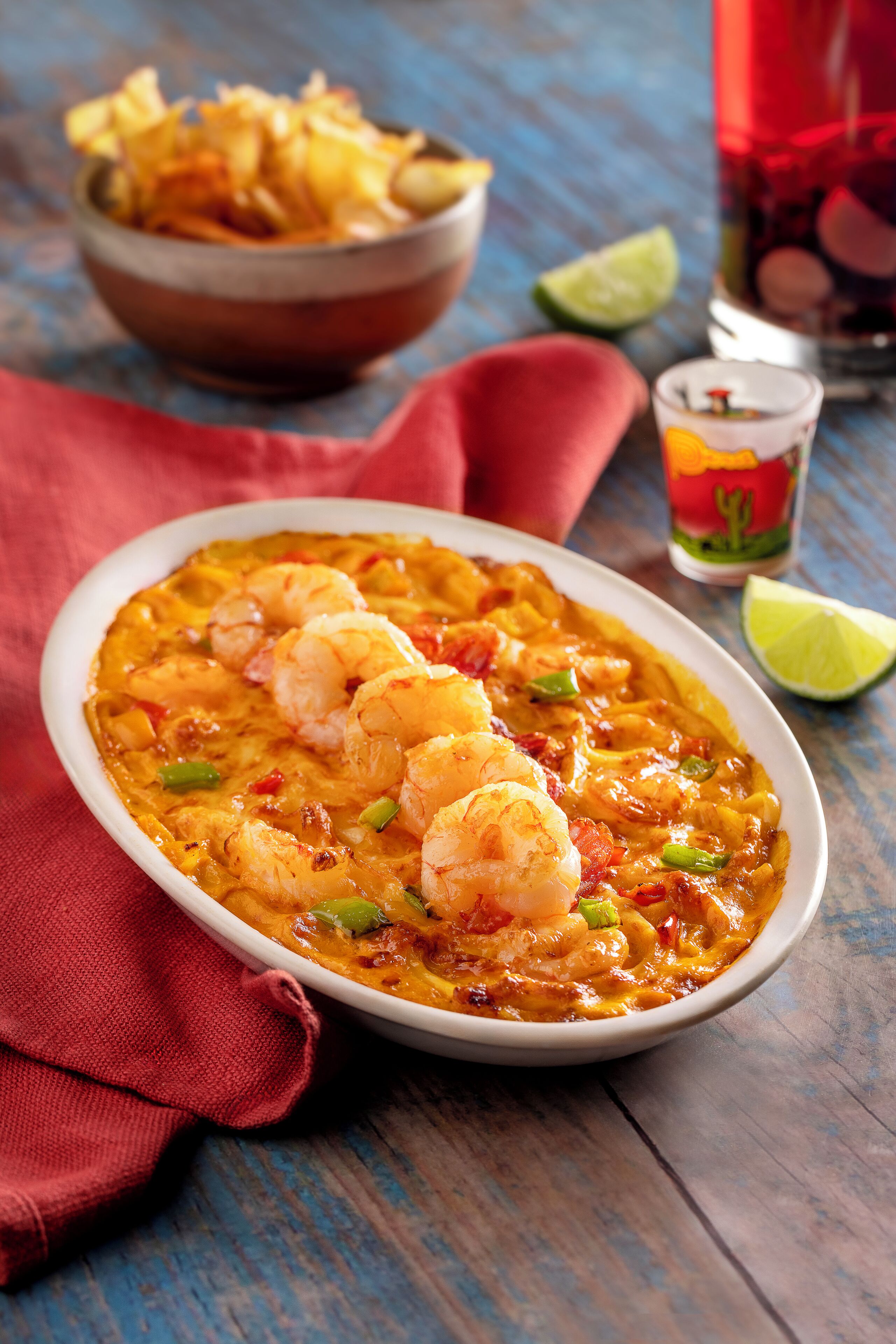 A bowl of shrimp and vegetable stew on a wooden table with a red cloth.
