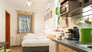 A compact hotel room with a bed, kitchenette, and a small dining area. - Oázis Apartmanok (Morahalom)