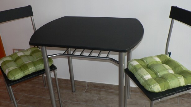A small, dark-colored table with two metal chairs, each with a green and white checkered cushion. - Oázis Apartmanok (Morahalom)