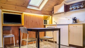 A compact kitchen with wooden cabinetry, a dining table with two chairs, a built-in oven, and a microwave. - Oázis Apartmanok (Morahalom)