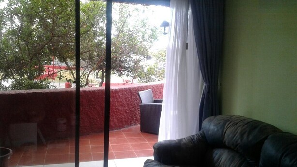 Habitación con puerta corrediza de vidrio que da a un espacio exterior con pared roja, una silla de mimbre y una mesita.
