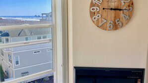 A room with a large window offering a view of buildings and a beach. A wooden clock with numbers is mounted on the wall. - Rockaway Shores (Rockaway Beach)