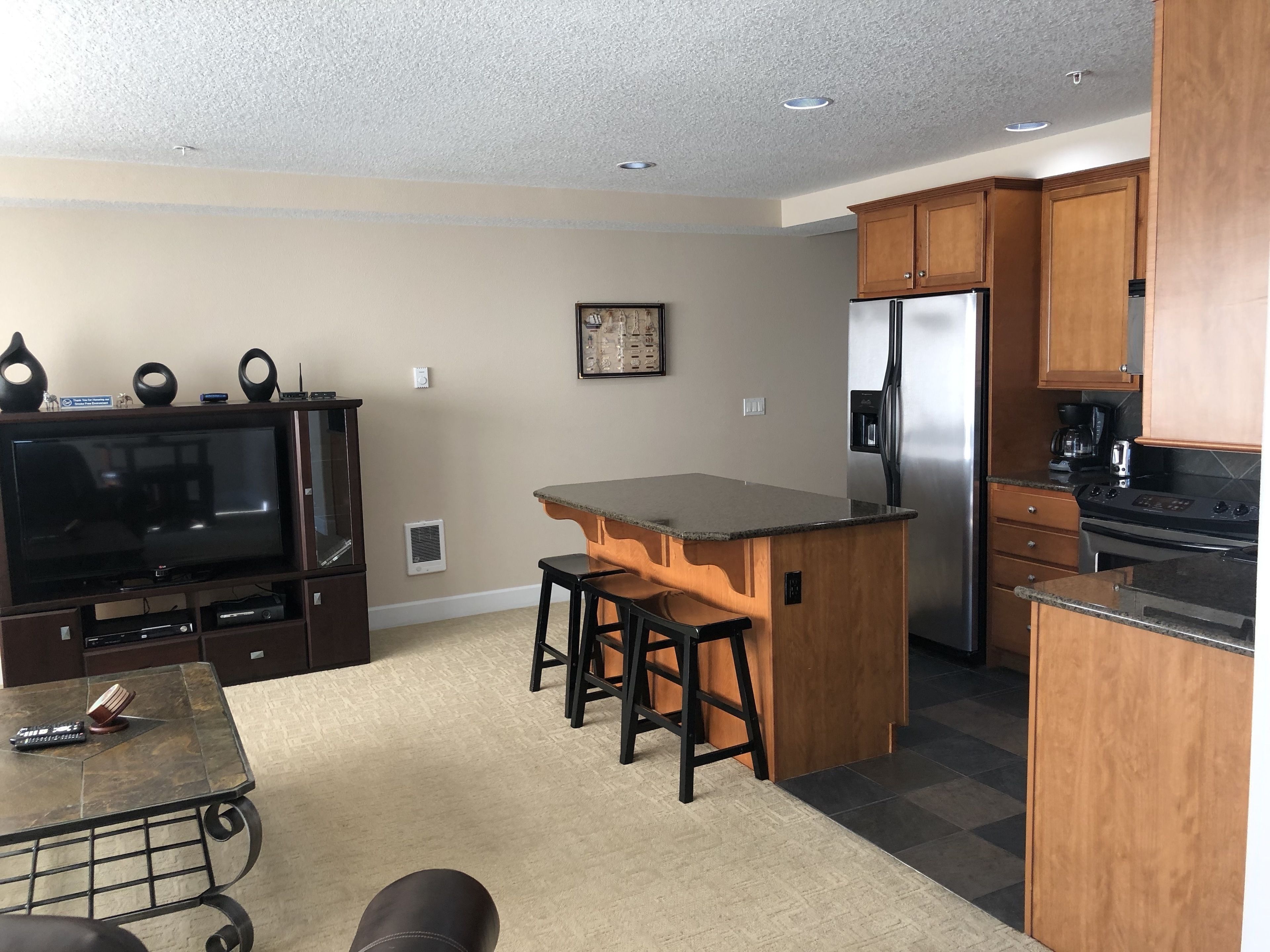 A compact kitchen with a built-in refrigerator, a dining area with stools, and a TV on a stand.