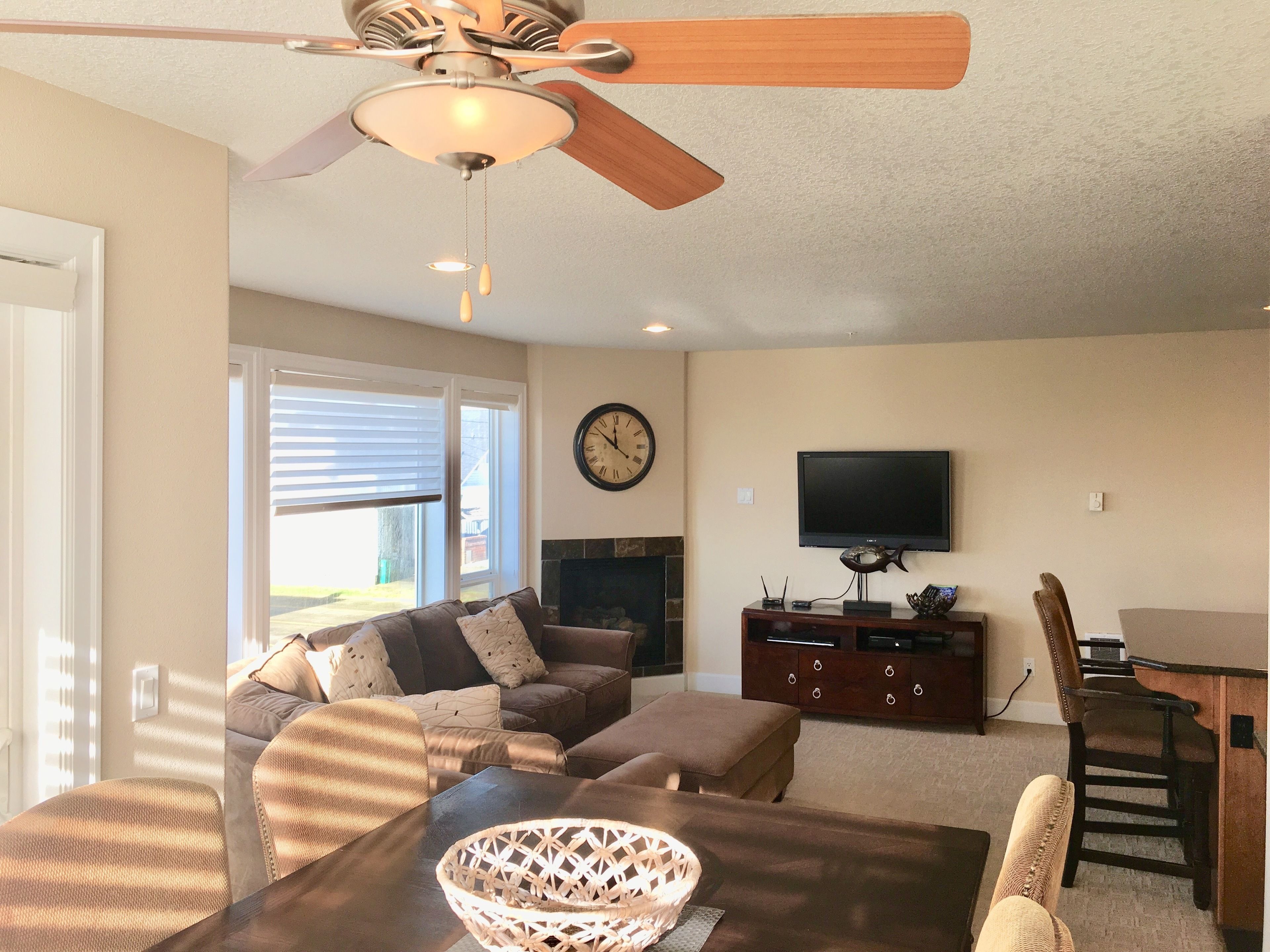 A living room with a ceiling fan, a fireplace, a television, and a dining area.
