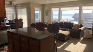 A spacious living area with a large window overlooking the beach, a cozy seating arrangement, and a kitchen area. - Rockaway Shores (Rockaway Beach)