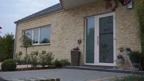 A stone building with a large glass door and windows, a small garden with plants, and a bicycle parked outside. - B&B De Watering (Lommel)