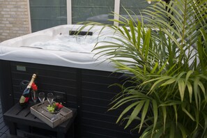 Un jacuzzi con una botella de champán, copas y una bandeja con fruta.