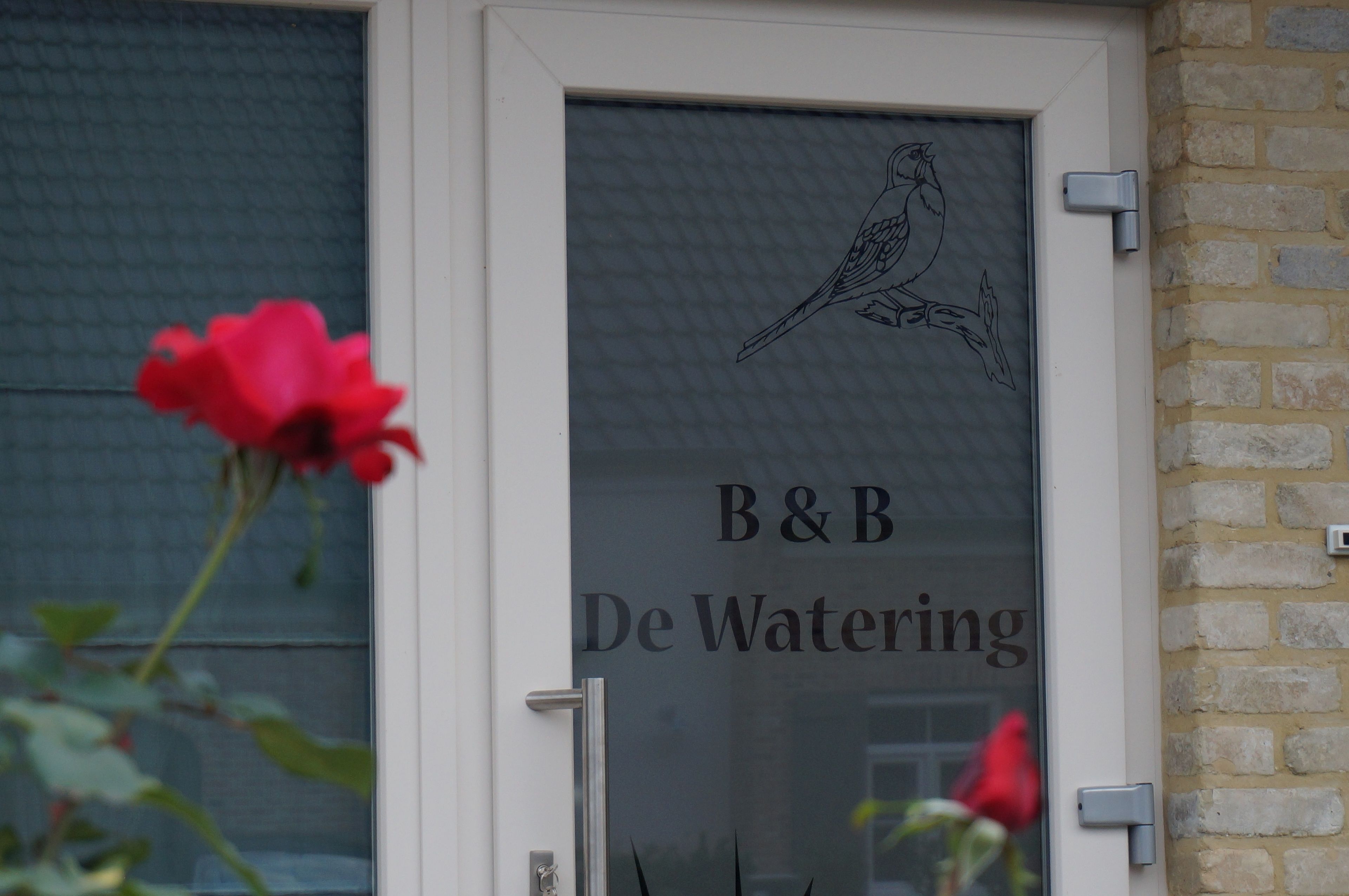 Een deur met een geëtste glazen ruit waarop een vogelafbeelding staat en de tekst 'B&B De Watering'.