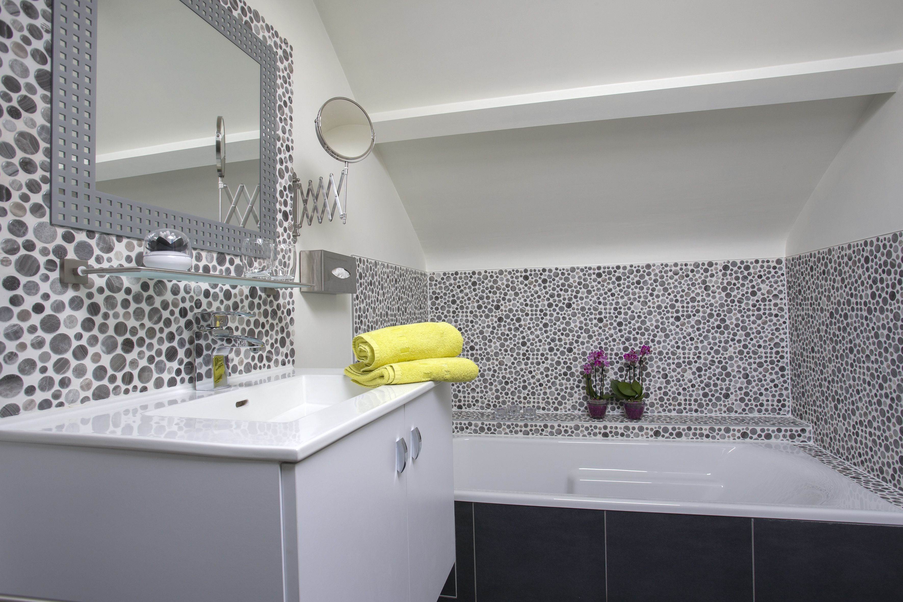 Ein modernes Badezimmer mit einem weißen Waschtisch, einer Badewanne und einer gefliesten Wand mit einem kreisförmigen Muster.