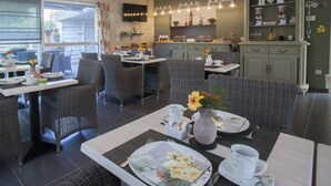 A dining area with wicker furniture, a kitchen in the background, and a TV mounted on the wall. - B&B De Watering (Lommel)