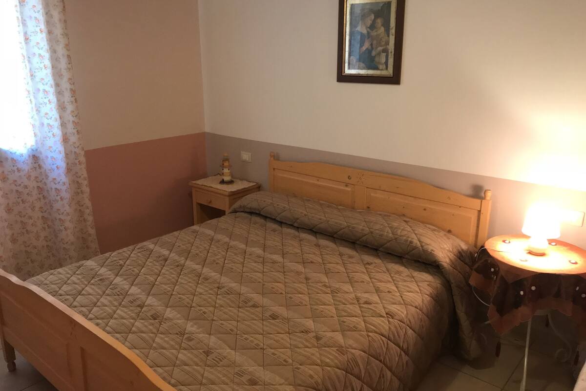 A bedroom with a wooden bed, a nightstand with a lamp, and a framed picture on the wall.
